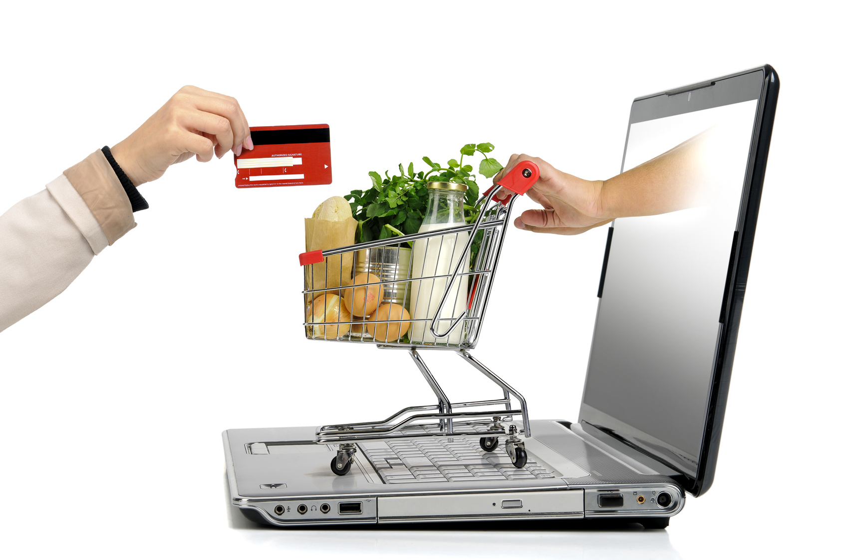 Hand with credit card and a small shopping cart coming from laptop screen isolated in white