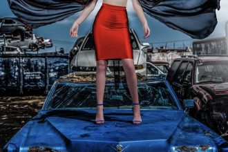 yas gonzalez fashion shoot. a model stands on a blue car, a cape flying out on the wind