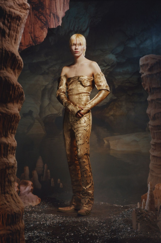 Man dressed in sparkly gold outfit against a cave backdrop
