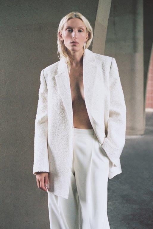 Woman with blond hair is wearing a matching white blazer and pants set