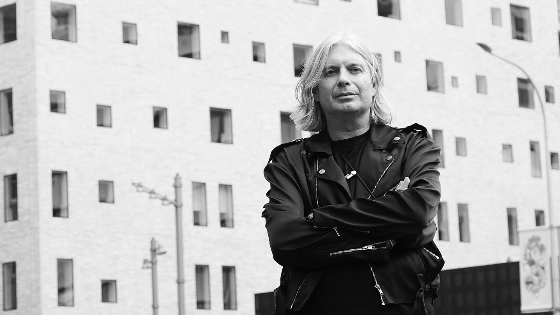 Black and white image of man with his arms crossed in front of a commercial building.