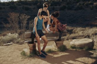Three runners sit on a wooden bench in the desert wearing outfits that colour coordinate with their shoes
