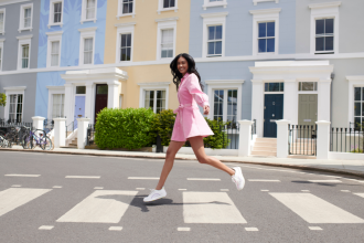 Woman in pink dress crosses road in front of pastel coloured town houses