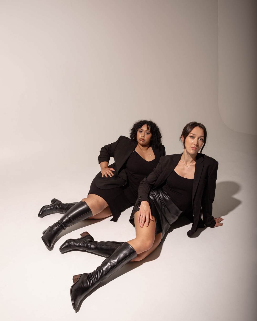 Two models laying on the ground wearing knee high boots and black blazers. Luxury Brand Expands Size Range. Luxury Brand Expands Size Range