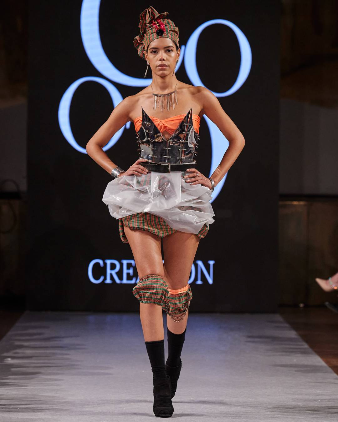 A model with a leather corset, plastic skirt and crazy hair walking down the runway.