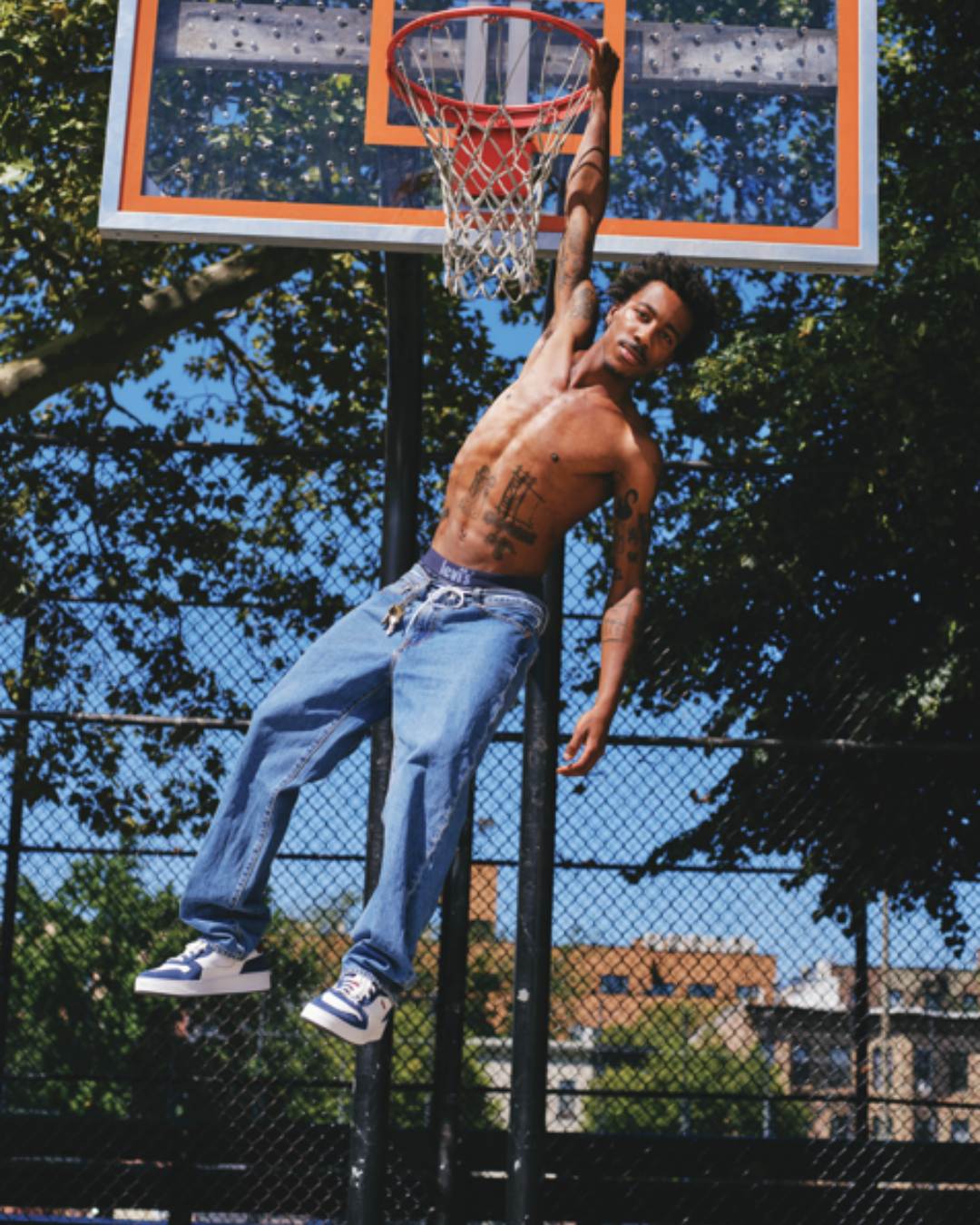 A man hanging from a basketball hoop. He is wearing a pair of Levi's baggy jeans.