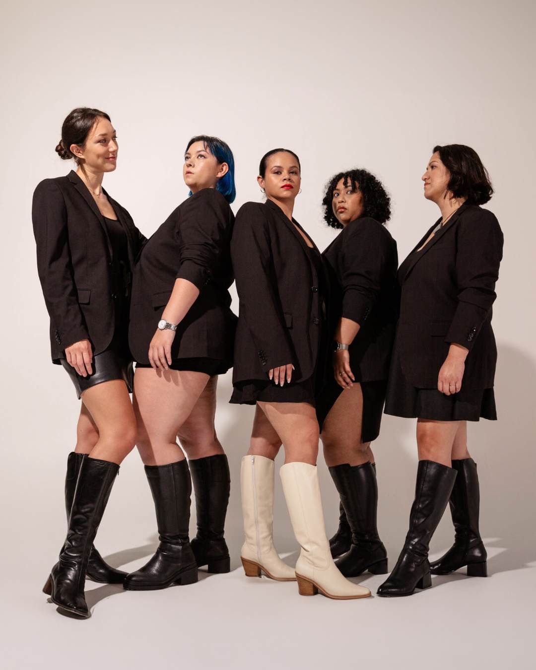 A group of women wearing black knee high boots. The woman in the middle is wearing white knee high boots. Luxury Brand Expands Size Range