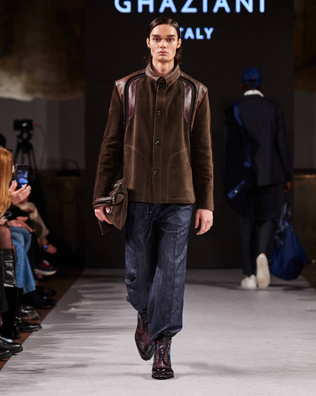 A man wearing a brown leather jacket. He is wearing denim jeans.