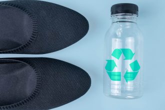 A pair of ballet flats next to a bottle with a recycling sign. The shoes are sustainable.