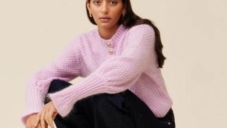 A woman wearing a purple knit cardigan, gold hoops and black jeans.